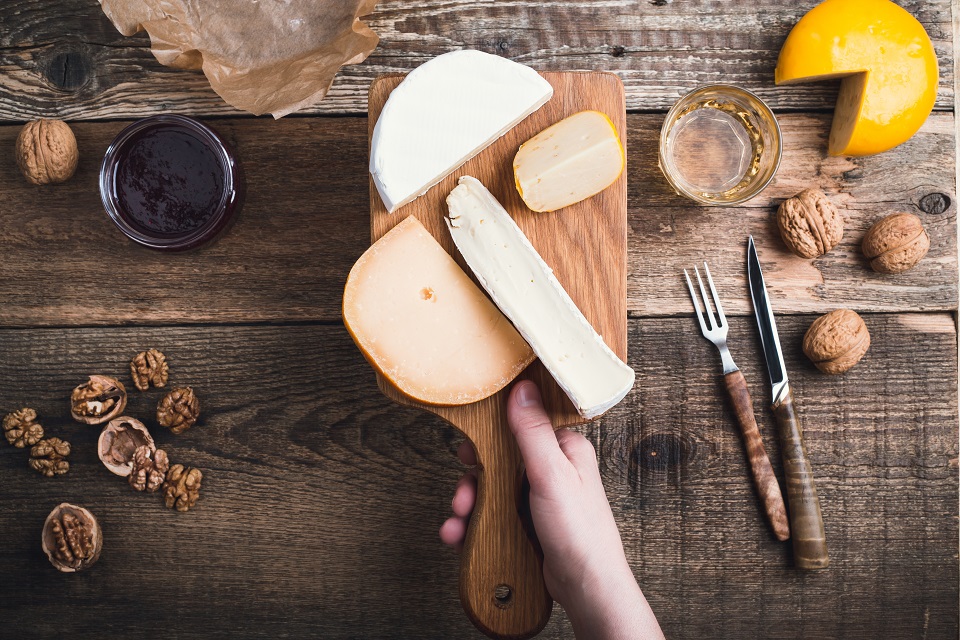 Close up hand holding cutting board with cheese, snack food on rustic table viewed from above