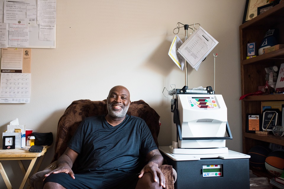 A man setting in a chair beside home hemodialysis machine.