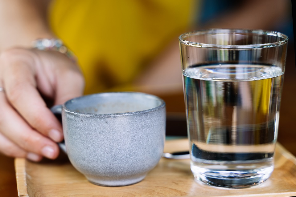 Hand holding a cup of coffee served with a glass of water and a spoon on a wooden plate on a wooden table